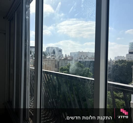 חלון אלומיניום עם נוף חיצוני של בניינים ועצים